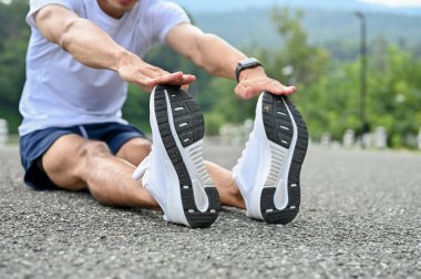 Spor giyim ve koşu ayakkabıları giymiş aktif ve yakışıklı Asyalı sporcu. Açık havada koşmadan önce bacaklarını esnetip ısınıyor. kırpılmış resim