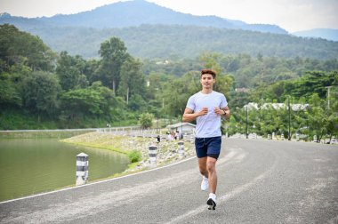 Sağlıklı ve aktif milenyum Asyalı adam spor kıyafetleriyle koşuyor ya da güzel gölde koşuyor, uzun maratondan önce antrenman yapıyor. Sağlıklı yaşam tarzı kavramı