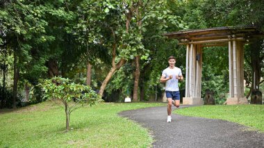 Aktif ve sağlıklı spor giyimli Asyalı bir adam güzel yeşil parkta koşuyor. eğitim, egzersiz, egzersiz konsepti