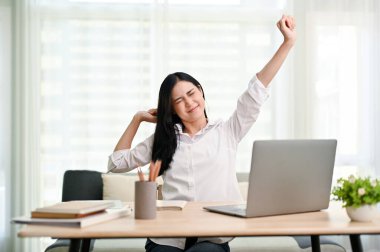 Yorgun ve yorgun Asyalı genç iş kadını ya da masa başında kollarını açıp işten sonra dinlenen kadın ofis çalışanı..