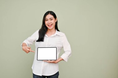 Beyaz tişörtlü güzel bir Asyalı kadın gri arka planda duran dijital tablet beyaz ekran modelini işaret ediyor. Tavsiye ya da öneri.