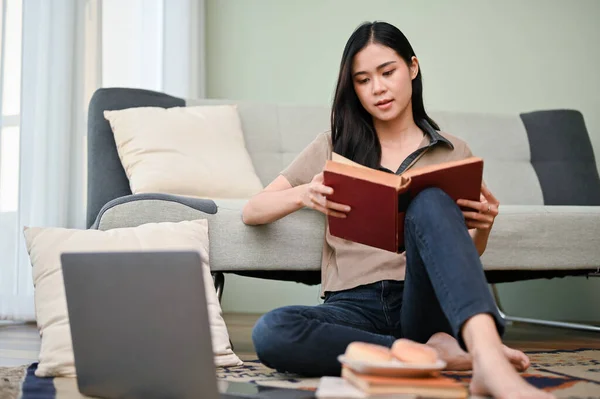 有魅力的年轻亚洲女人在客厅看书 研究课本信息 做大学作业 — 图库照片