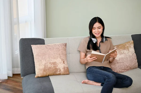 迷人的年轻亚洲女性穿着休闲装 一边看书 一边在客厅的沙发上休息 活动和休闲概念 — 图库照片