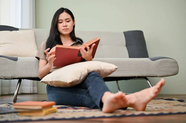 迷人的年轻亚洲女人在客厅里放松的同时 专心致志地看书或课本 休闲概念 — 图库照片