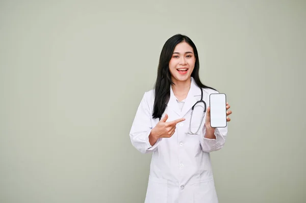 灰色の背景に立って スマートフォンの白い画面のモックアップで統一された指差し指で美しいアジアの女性医師 緊急連絡先 医療プログラム 病院のアプリケーション — ストック写真