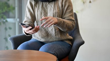 Kafede oturan rahat kazaklı genç bir Asyalı kadın akıllı telefon kullanarak arkadaşlarına mesaj atıyor. kırpılmış resim