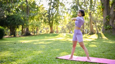 Sağlıklı ve aktif milenyum Asyalı kadın spor kıyafetleriyle vücudunu yoga minderinde esnetiyor, yeşillik bahçesinde kardiyo antrenmanı yapıyor..