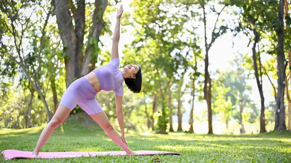健康而活跃的年轻亚洲女子穿着运动服在绿色的自然花园里运动 练习三角前倾瑜伽姿势 福利生活方式概念 — 图库照片
