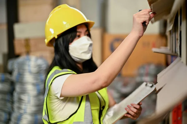 プロの若いアジアの女性の産業労働者や倉庫労働者が均一で堅い帽子在庫をチェックし 倉庫で働く — ストック写真