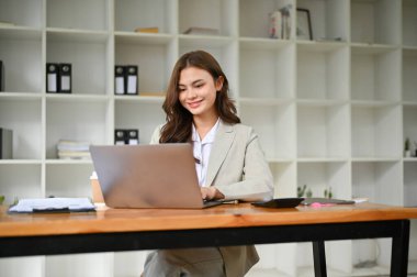 Çekici ve çekici beyaz iş kadını ya da takım elbiseli kadın pazarlama müdürü dizüstü bilgisayarına bakıyor, dizüstü bilgisayar kullanıyor, modern ofisinde çalışıyor..