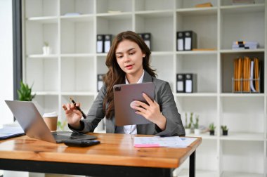 Ofisindeki görevlerine odaklanan, dijital tabletine bakan, projesini düşünen ve planlayan çekici beyaz bir iş kadını..