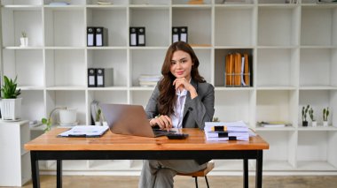 Çekici ve çekici beyaz iş kadını ya da takım elbiseli kadın CEO 'su, masasında elleri çenesinde oturuyor, gülümsüyor ve kameraya bakmıyor. Düşünüyor, düşünüyor, hayal kuruyor..