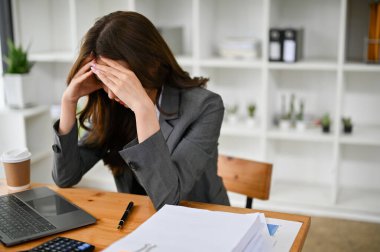 Stresli ve üzgün Asyalı genç iş kadını ya da masasında oturan bayan ofis çalışanı, baş ağrısı, akıl sağlığı bozuk, depresyonda, çalışmaktan bıkmış..