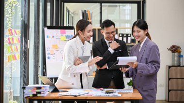 İki profesyonel ve memnun Asyalı iş adamı, genç bir pazarlama çalışanının proje detaylarını incelemek üzere panoya bakıyorlar..