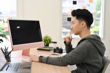 Zeki ve yakışıklı Asyalı bir üniversite öğrencisi ya da masasında çalışan bir ofis çalışanı, bilgisayarına odaklanmış..