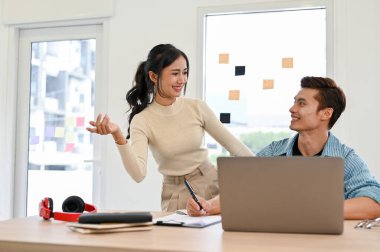 Mutlu ve neşeli Asyalı genç erkek ve kadın pazarlama bürosu çalışanları birlikte çalışırken, fikir alışverişinde bulunurken sohbetin tadını çıkarıyorlar..