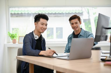 Ofiste birlikte çalışan iki profesyonel Asyalı genç erkek programcı ya da fotoğraf editörü beyin fırtınası yapıyor ve tartışıyorlar..