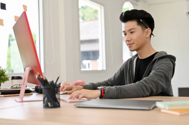 Zeki Asyalı genç erkek programcı ya da ofis çalışanı ofis masasında çalışıyor, proje ödevi üzerinde çalışıyor..