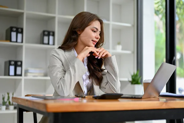 stock image Gorgeous and professional young caucasian businesswoman or female boss in business suit thinking and planning her new project on laptop, working in the office.