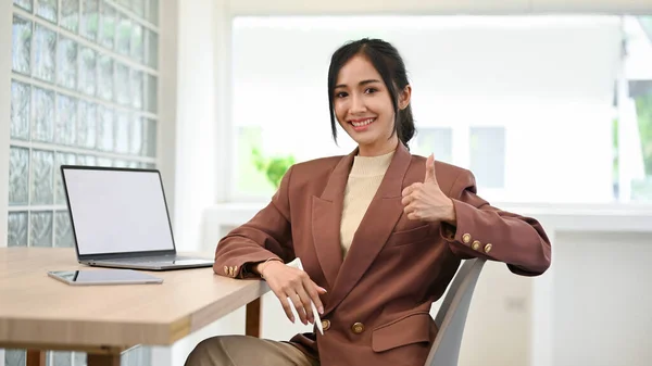 迷人的年轻亚洲女商人或穿着西装的女经理坐在她的办公桌前 竖起大拇指 微笑着看着镜头 伟大的工作 — 图库照片