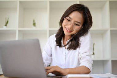 Güzel Asyalı kadın sekreter ya da asistanı ofis masasında çalışıyor, iş müşterisiyle telefonda konuşuyor ve bilgisayarına bilgi yazıyor..