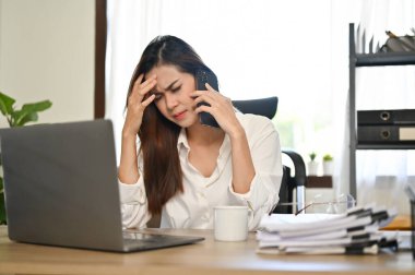 Stresli Asyalı iş kadını ya da bayan patron masasında oturmuş iş ortağıyla telefonda ciddi bir konuşma yapıyor..