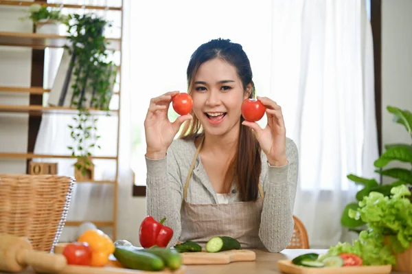 迷人而年轻貌美的亚洲女人拿着西红柿 笑着看着相机 喜欢在厨房里做沙拉碗 — 图库照片