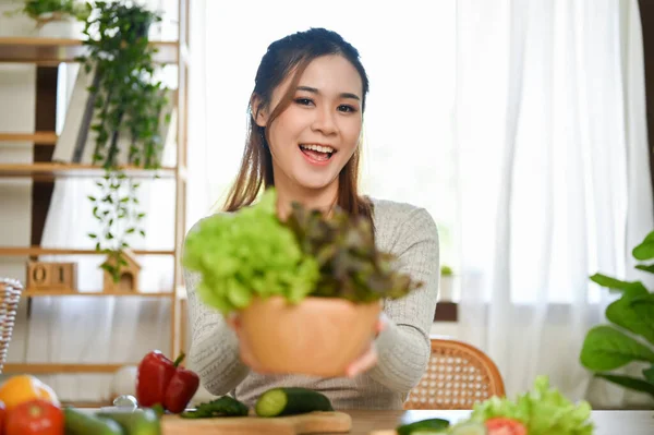 美丽而健康的年轻亚洲女性坐在餐桌旁 手里拿着一个新鲜的沙拉蔬菜碗 在厨房里煮着沙拉碗 — 图库照片