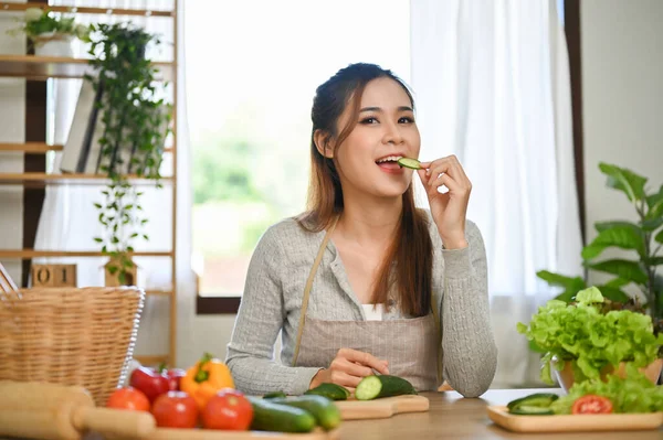迷人的年轻亚洲女性吃着一片黄瓜片 喜欢在厨房里为她的健康饮食准备配料 福利生活方式概念 — 图库照片