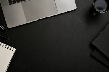 Modern ofis masası üst görünümü, ortadaki metin görüntüsü için düz yatay dizüstü bilgisayar, kahve fincanı, kitaplar ve siyah arkaplan üzerine kırtasiye.