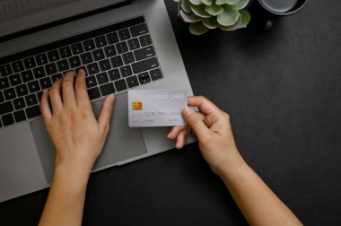 Üst görünüm, modern stil siyah ofis masası, kredi kartı tutan ve dizüstü bilgisayarda yazan bir kadın eli, kredi kartı ödemelerini web sitesine kaydet. çevrimiçi alışveriş kavramı