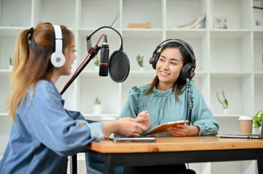 İki mutlu ve neşeli Asyalı kadın podcaster çevrimiçi radyo şovlarını birlikte yürütüyor, başlıkları hakkında konuşuyor ve fikirlerini paylaşıyorlar..