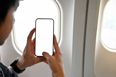 Genç Asyalı erkek yolcu ya da yolcu uçuş sırasında güzel bir gökyüzünün fotoğrafını çekmek için akıllı telefonunu kullanıyor. yakın plan görüntü, telefon beyaz ekran modeli.