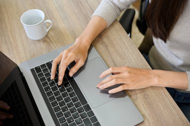 Dizüstü bilgisayar kullanan, klavyede yazan, internette gezinen, online görevleri üzerinde çalışan bir iş kadını ya da kadın serbest çalışan. Üst görünüm, yakın çekim eller resmi