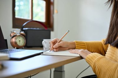 Genç Asyalı bir üniversite öğrencisi ödev yapıyor, okul defterine kalemle yazıyor, günlüğünü masasında yazıyor. yakın plan resim