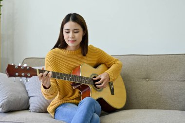 Yetenekli ve profesyonel Asyalı bayan müzisyen ya da gitarist akustik gitarını en az oturma odasında çalıyor. hobi ya da eğlence konsepti