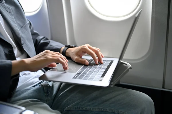 A businessman passenger using his laptop computer, working on his business task during travel on the plane. cropped image