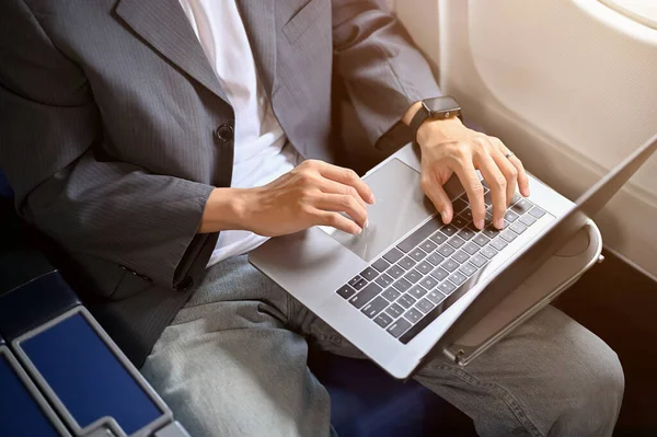 A professional businessman in formal suit is working on his project, using portable notebook laptop during the flight to his business trip. cropped image