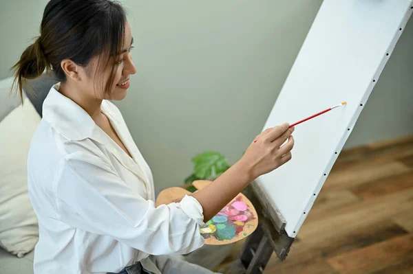 stock image Talented and professional Asian female painter or artist designing her artwork on a canvas easel and painting with acrylic color in her studio.