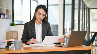 Profesyonel ve başarılı Asyalı iş kadını evrak işlerine odaklanıyor, ofisindeki masasında çalışıyor..