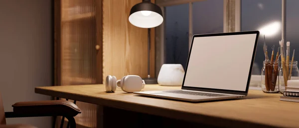 Cozy Scandinavian home workspace with laptop blank screen mockup, light from table lamp, headphones, painting tools on wood table. close-up image. 3d render, 3d illustration