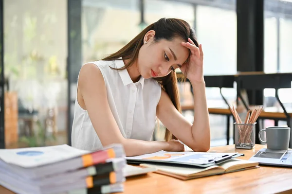 Stressed and frustrated millennial Asian businesswoman or female boss upset with her work, worried about her project\'s result, working at her desk. depressed, headache, problem, trouble