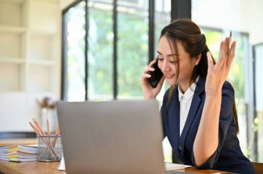 Güzel ve profesyonel Asyalı iş kadını müşterisiyle telefonda konuşuyor, masasında çalışırken telefonla iş anlaşması yapıyor..