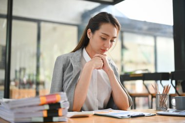 Profesyonel ve düşünceli Asyalı iş kadını görevlerine odaklanıyor, rapordaki mali verileri analiz ediyor, masasında çalışıyor..