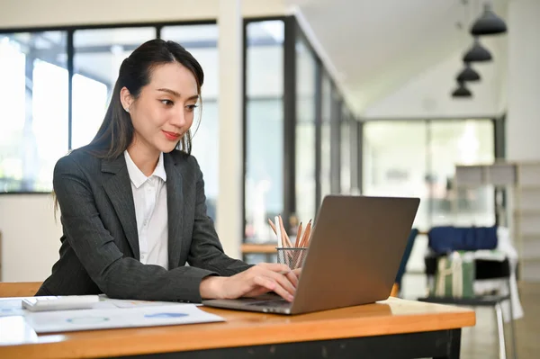 Professional and attractive young Asian female accountant or financial worker using laptop computer, typing on keyboard, working in her office.