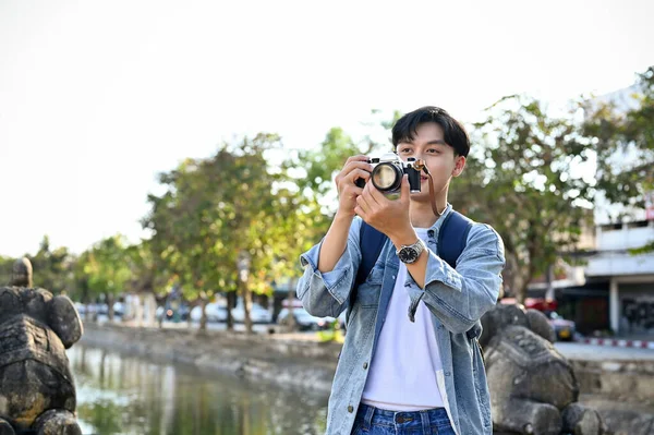 都会の散策を楽しみながらレトロなカメラで写真を撮りながらジャンジャケット姿の幸せとハンサムな若いアジアの男性旅行者 — ストック写真
