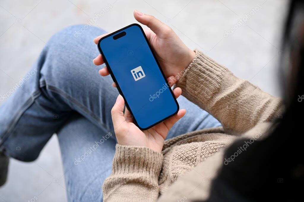 Chiang Mai, Thailand - Nov 25 2022: A female hand holding a smartphone with Linkedin application logo on screen. resume, job, career, internship
