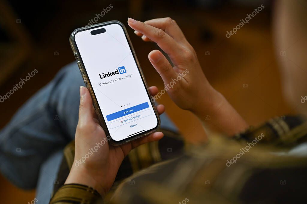 Chiang Mai, Thailand - Nov 24 2022: A female using her smartphone, holding a smartphone with Linkedin logo on screen. Job and internship platform