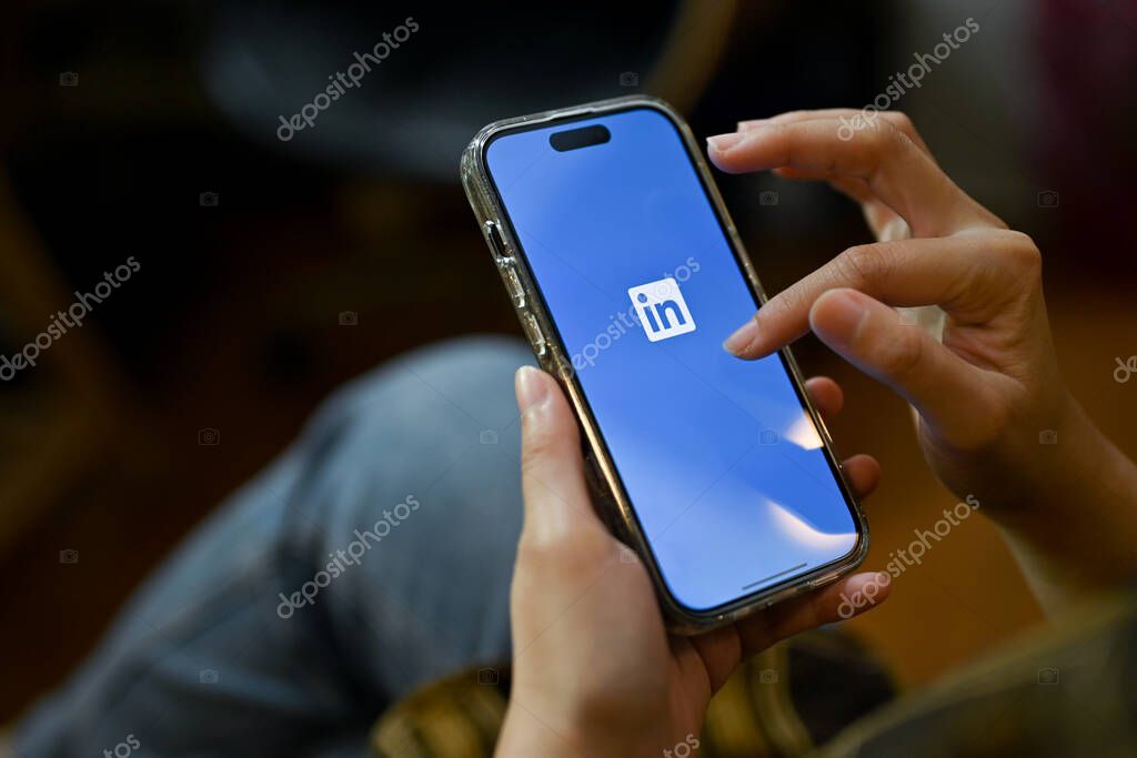 Chiang Mai, Thailand - Nov 24 2022: A female using her smartphone, holding a smartphone with Linkedin logo on screen. Job and internship platform, employment, finding a job