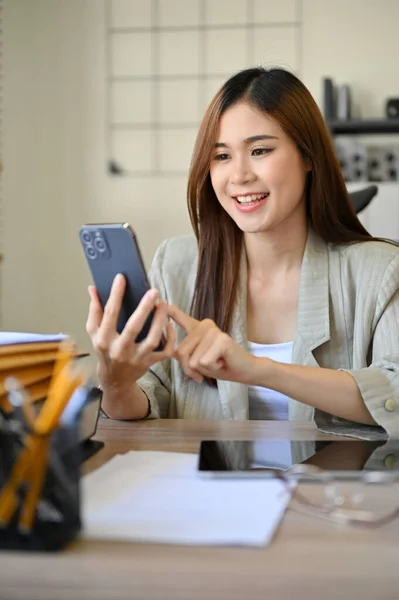优雅的千年亚洲女商人或办公室女职员坐在办公桌前 用智能手机与朋友聊天 上网购物和发邮件 — 图库照片